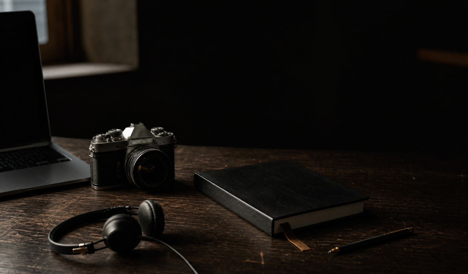 A notebook, camera and headphones on a dark creative studio desk